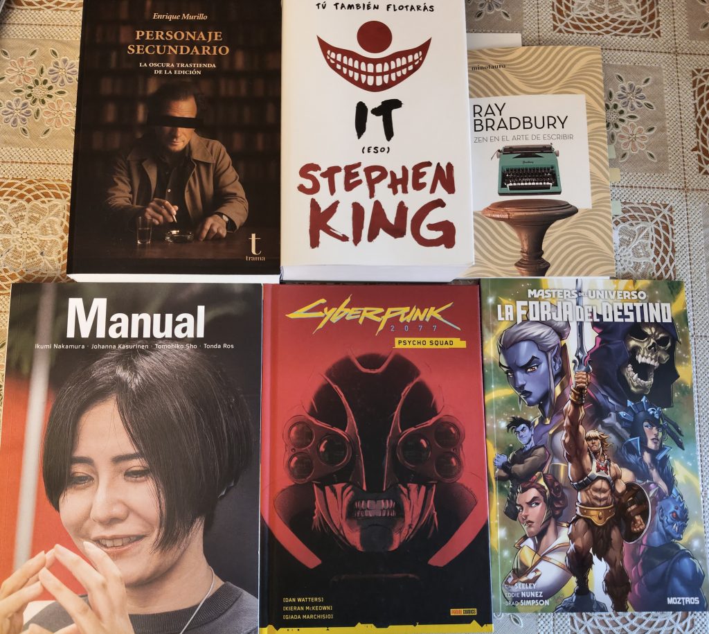 Foto de los libros que pretendo leer durante diciembre. Están puestos sobre una mesa en dos filas.
En la fila superior están los libros PErsonaje Secundario de Enrique Murillo, It de Stephen King y Zen en el arte de escribir de Ray Bradbury. 
En la segunda fila están la revista manual número 16, el comic Cyberpunk 2077 Psycho Squad y el cómic Masters del Universo La Forja del Destino