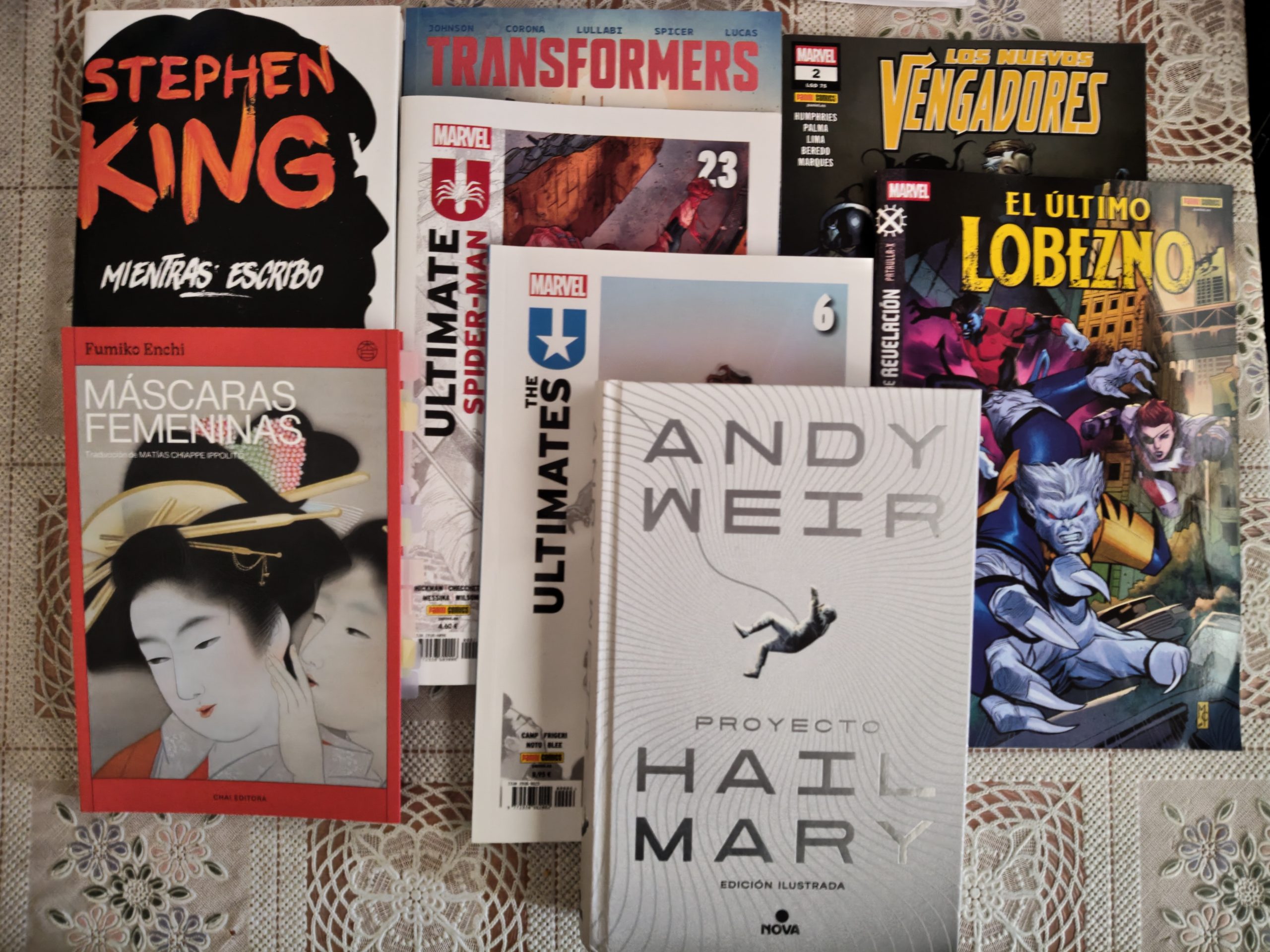 Fotografía de una serie de libros y cómics apilados mostrando el títulos de todos aunque no las portadas completas. Son: Mientras escribo, transformers 4, Nuevos vengadores 2, El último lobezno 2, Ultimate SPider-man 23, The Ultimates 6, Proyecto Hail Mary y Máscaras femenninas.