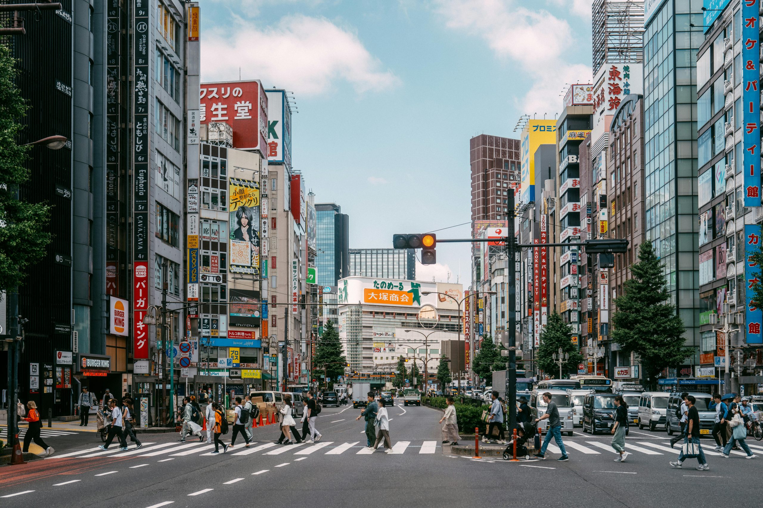 Fotografía real de una calle de Tokyo donde se ve a la gente cruzando por un paso de peatones y diversos coches parados esperando.